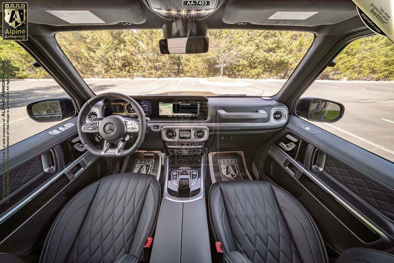 The interior of a bulletproof Mercedes G63 with quilted leather seats, a multifunction steering wheel, and a central dashboard display. The view is from the rear seat looking forward.