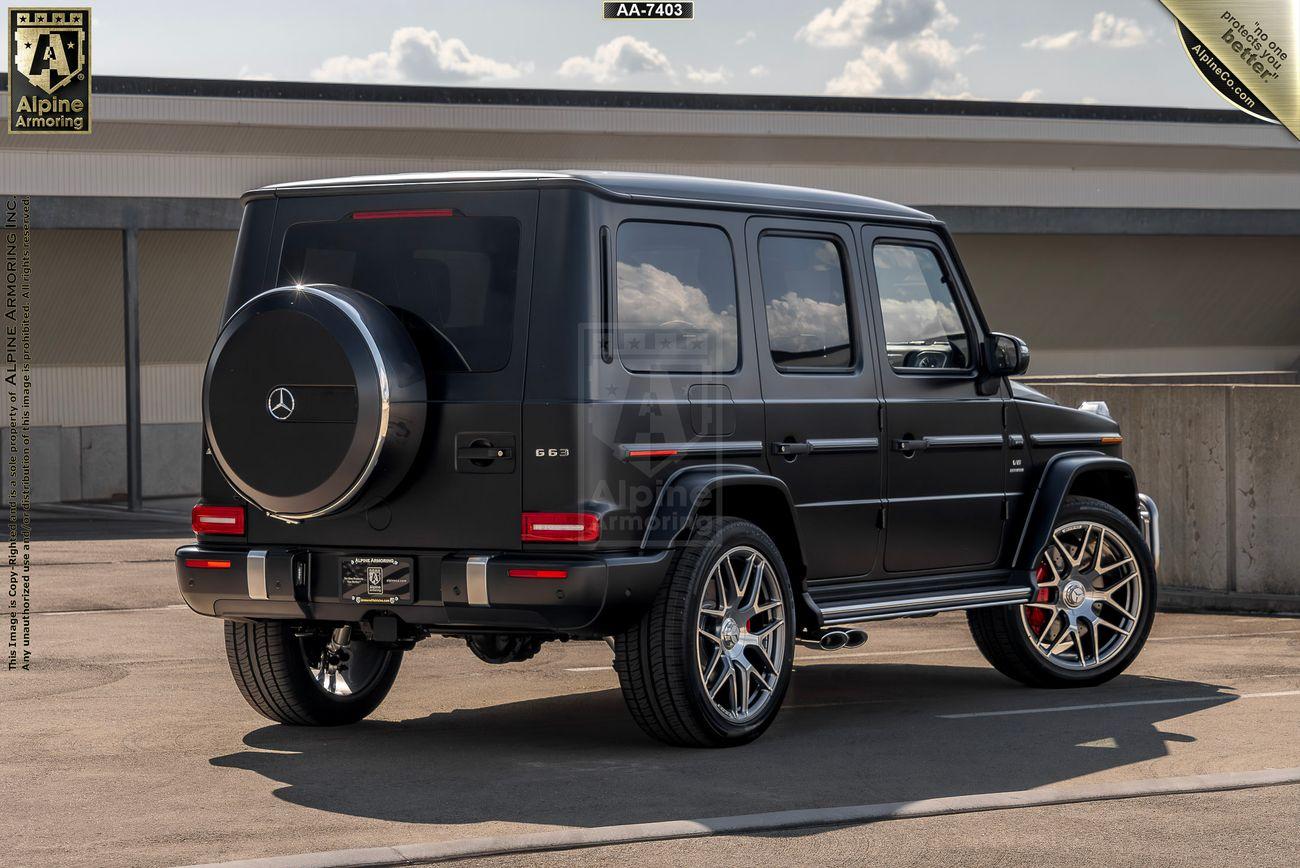 A black Mercedes-Benz G-Class SUV is parked on a rooftop with a clear sky background. The vehicle has large alloy wheels and a rear spare tire cover.