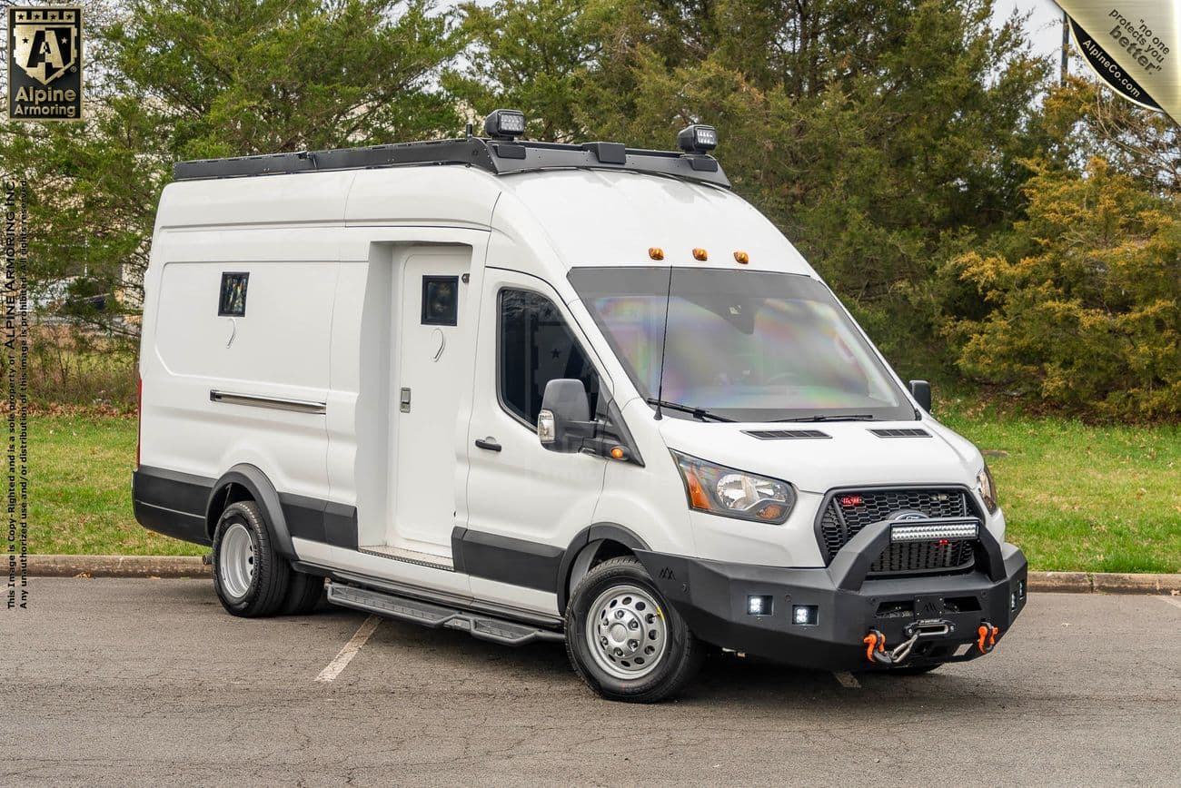 A white, customized Pointer van is parked on a paved area with green trees in the background. The van features a raised roof, off-road tires, and additional front bumper equipment.