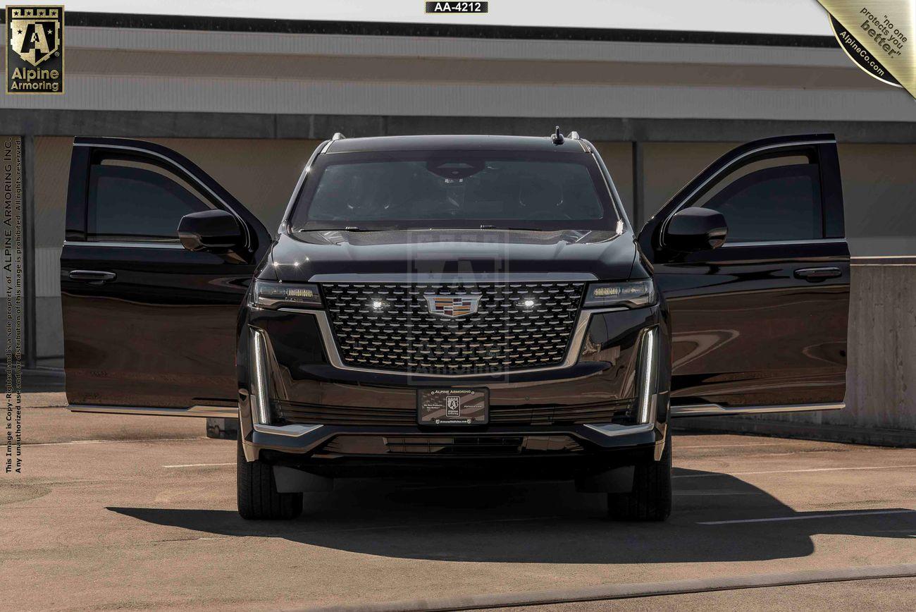 Front view of an armored Cadillac Escalade ESV SUV with both front doors open, displaying the vehicle's grille and headlights. The SUV is parked in an outdoor lot.