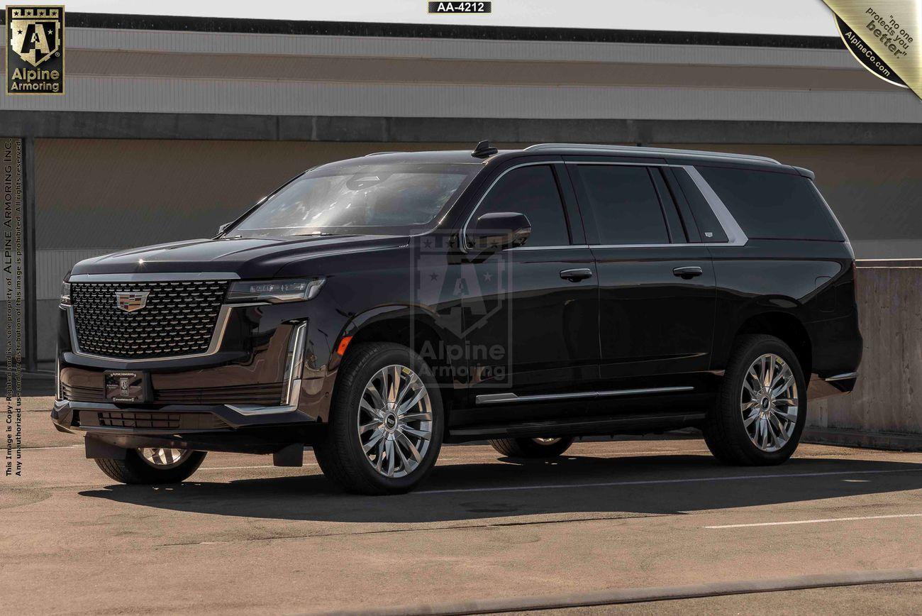 A black armored Cadillac Escalade ESV  with a Cadillac emblem on the grille is parked inA black armored Cadillac Escalade ESV  with a Cadillac emblem on the grille is parked in an outdoor area on a sunny day. an outdoor area on a sunny day.