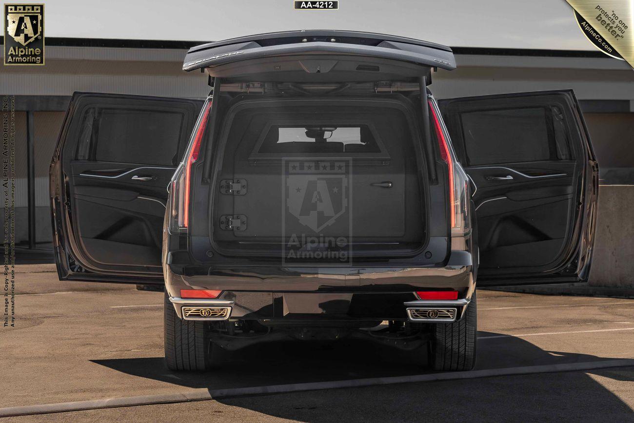 Rear view of a black armored Cadillac Escalade ESV SUV with open tailgate and rear doors, revealing a spacious cargo area. The vehicle is parked on a concrete surface.