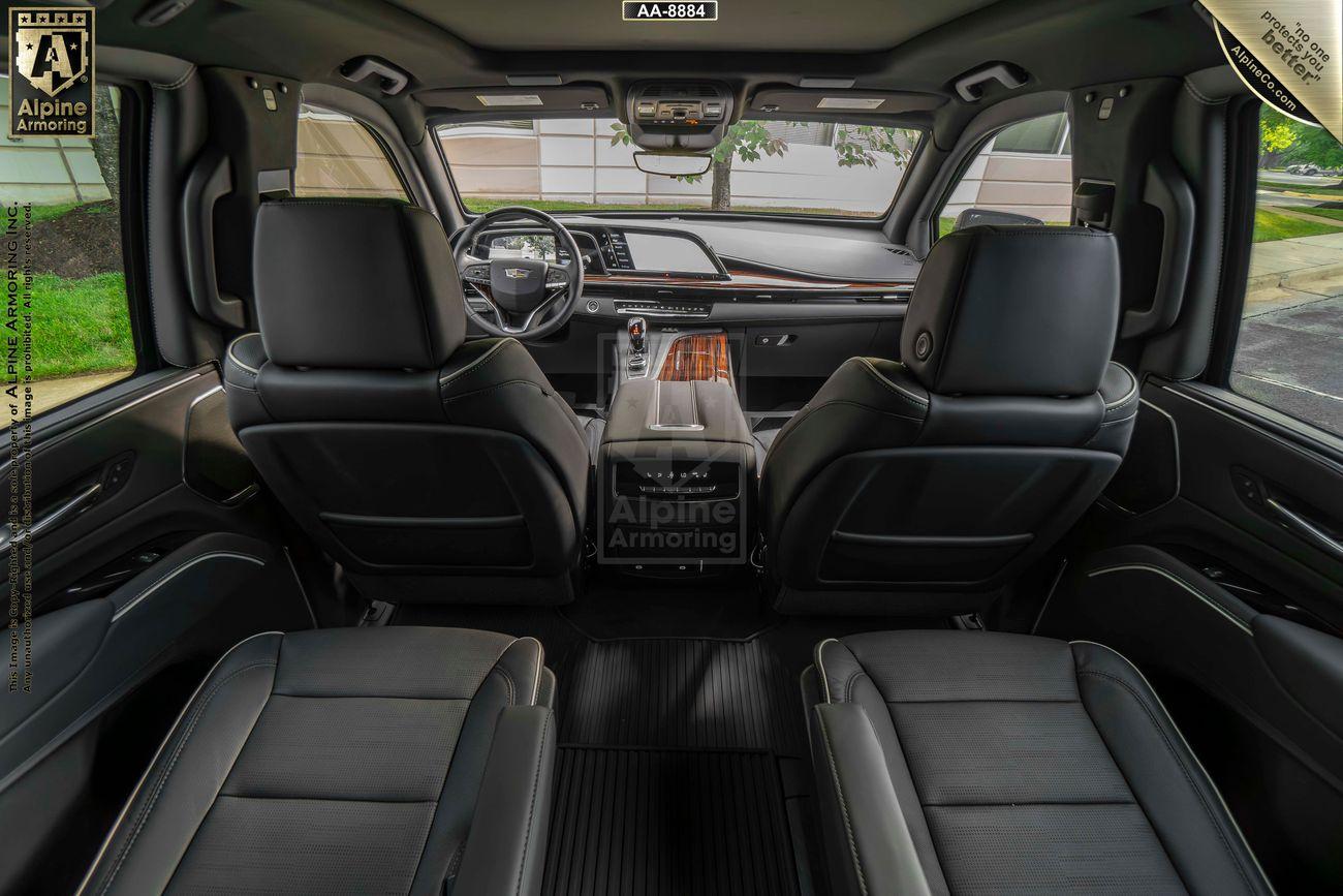 Interior view of an armored Cadillac Escalade Premium Luxury SUV with leather seats, showcasing the front dashboard, steering wheel, and rear passenger seating. A logo is visible on the center console.