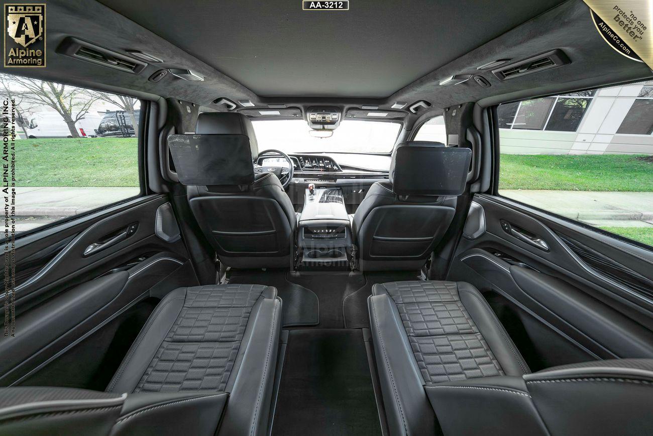 Interior view of an armored Cadillac Escalade ESV with four black leather captain's seats, large windows, and overhead lighting, showcasing modern and spacious design features.