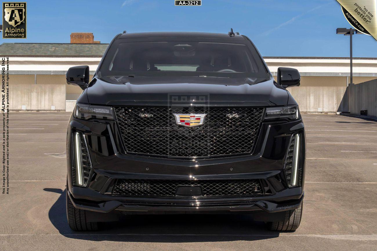 Front view of a armored Cadillac Escalade ESV SUV  parked in an empty lot under a clear blue sky.