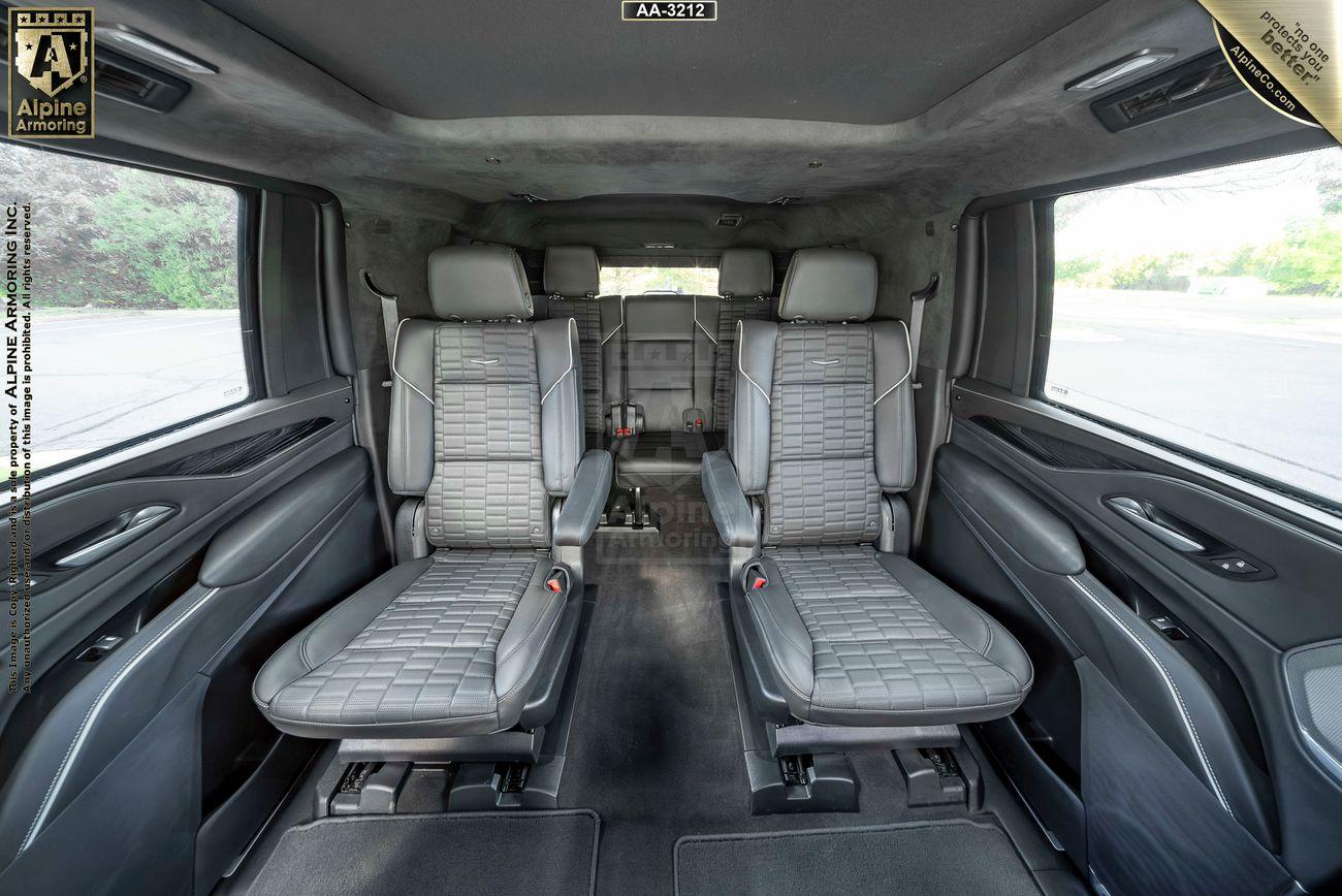 Interior of a Cadillac Escalade ESV SUV featuring two leather-trimmed captain seats in the middle row, with panoramic windows on either side and a spacious aisle between the seats.