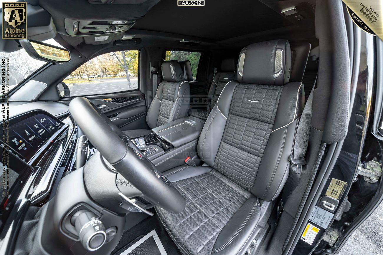 Interior of a luxurious armored Cadillac Escalade ESV SUV with black leather seats featuring intricate stitching, a modern dashboard, and various controls and displays.