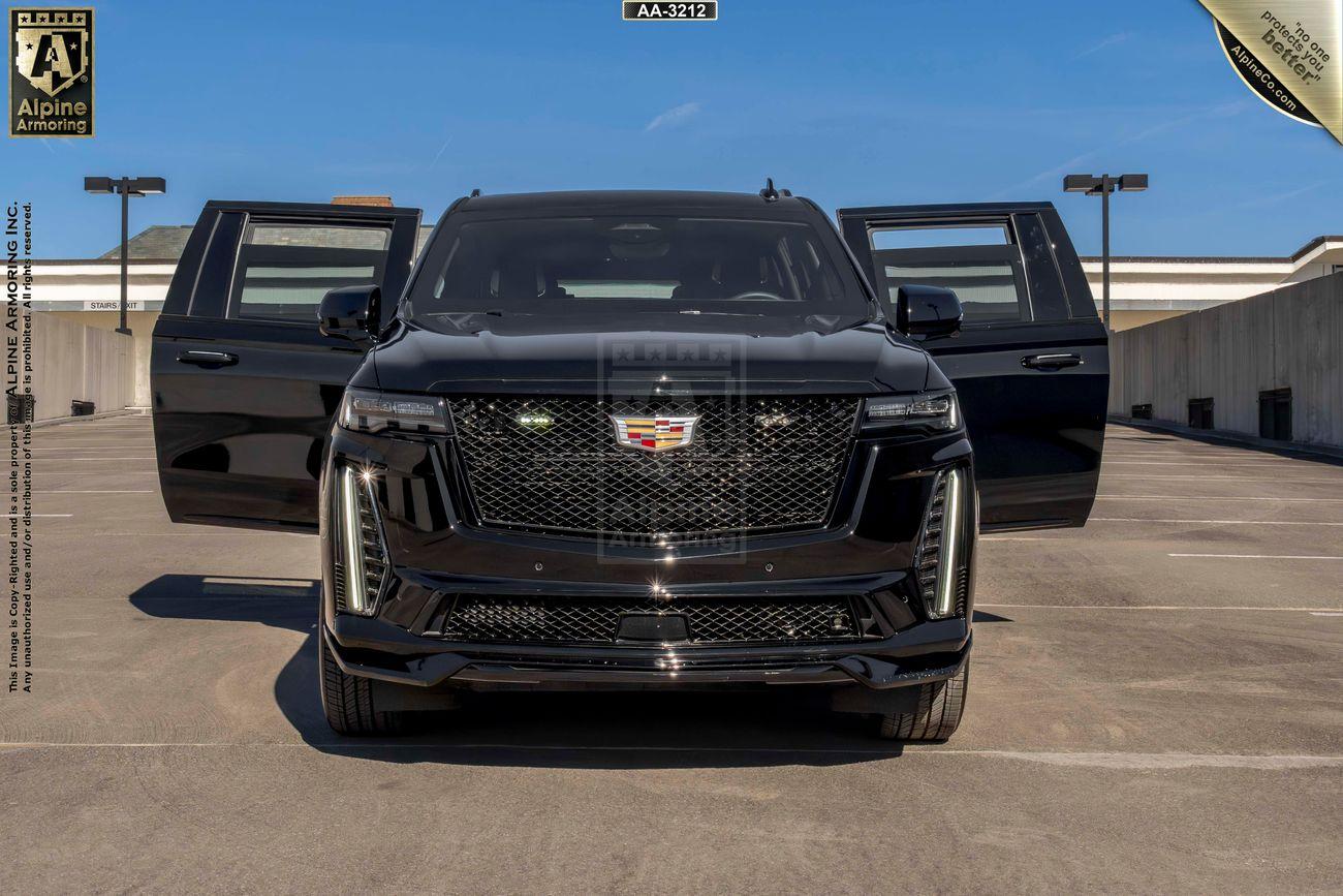 Front view of a black armored Cadillac Escalade ESV SUV with both front doors open, parked in an outdoor lot with a clear sky in the background.