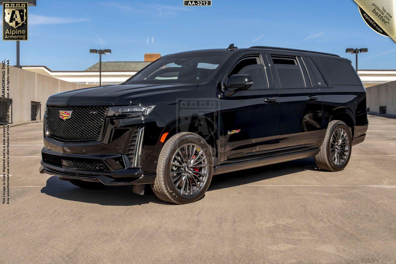 A black armored Cadillac Escalade ESV SUV is parked on a rooftop parking lot with a blue sky in the background.