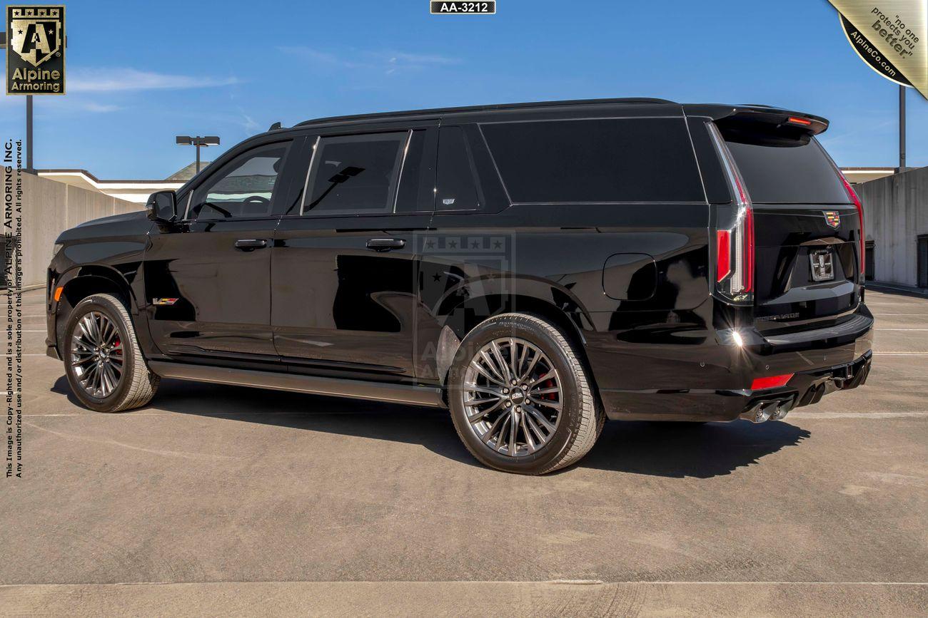 A black armored Cadillac Escalade ESV SUV is parked on a rooftop with surrounding buildings visible. The vehicle has tinted windows and chrome alloy wheels.