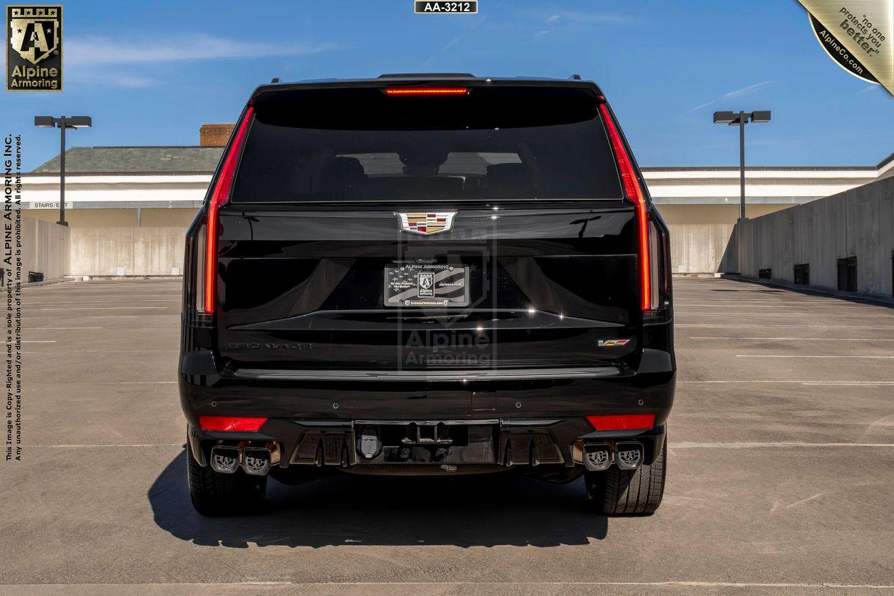 Rear view of a armored Cadillac Escalade ESV SUV  parked in an empty lot under a clear blue sky.