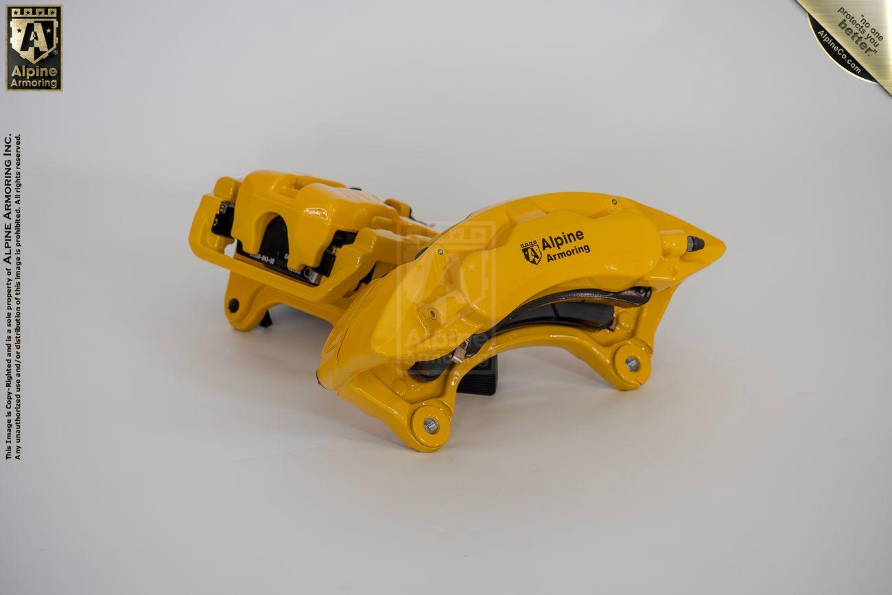 Two yellow brake calipers from Alpine Armoring, positioned side by side, showcasing their robust construction and advanced engineering for armored vehicles.