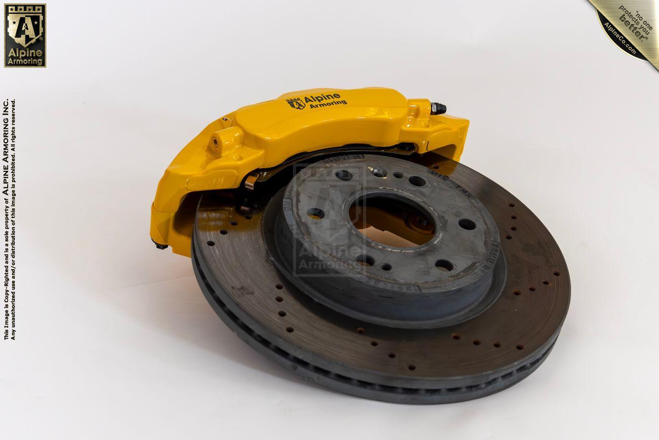 A yellow brake caliper from Alpine Armoring, shown from above, highlighting its robust construction and advanced engineering for armored vehicles.