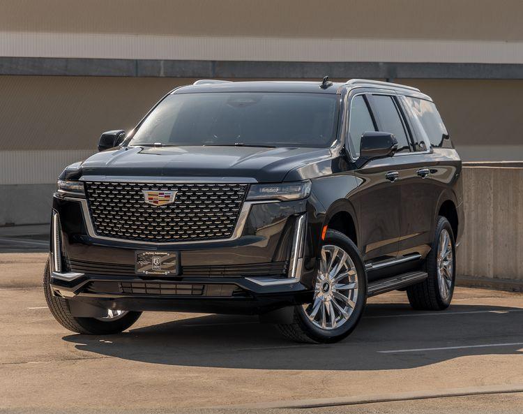 A black armored Cadillac Escalade SUV is parked in an urban outdoor setting, showcasing its front and side profile with prominent grille and sleek design.