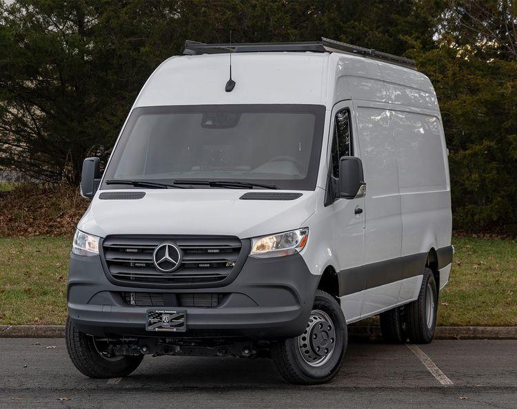 A white Mercedes-Benz Sprinter van is parked in an outdoor area with trees in the background.