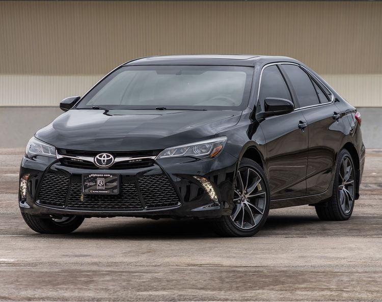 A black armored Toyota Camry is parked on a concrete surface. The car has dark tinted windows and a modern front grille design.