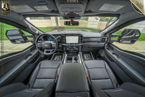 A view of the interior cabin of an armored Ford F-350 Lariat truck, showcasing a spacious dashboard with a large touchscreen display, steering wheel controls, and black leather seats.