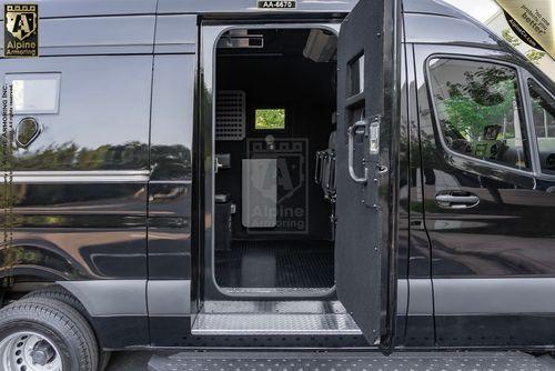 Black armored Pointer Van from Alpine Armoring with an open side door revealing its interior. The vehicle features visible Alpine Armoring logos on its exterior and interior.