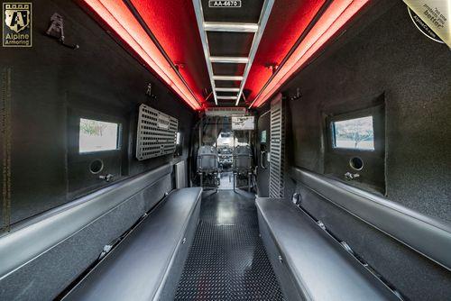 Interior of an armored Pointer Van from Alpine Armoring with grey seats and walls, a black floor, and red lighting along the ceiling. The vehicle is designed for secure transportation.