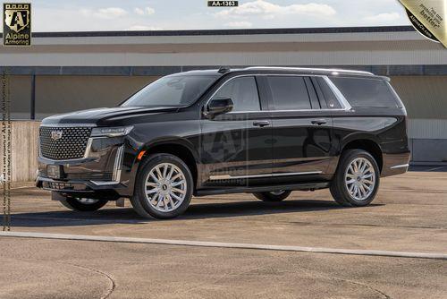 An armored black Cadillac Escalade Escalade ESV Luxury SUV is parked on a concrete surface, with a large building and blue sky in the background.