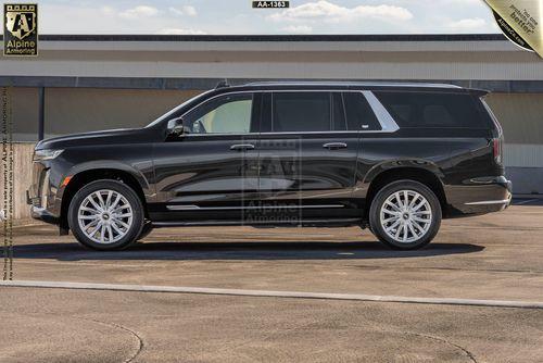 A black Cadillac Escalade ESV Luxury SUV is parked on a paved surface in front of a large building. The vehicle has silver rims and tinted windows.