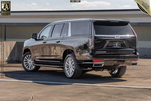 A black Cadillac Escalade ESV Luxury is parked outside in a large open area. The vehicle's rear and side are visible, showcasing its sleek design and prominent taillights.