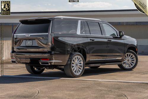 A black armored  Cadillac Escalade ESV Luxury SUV is parked on an outdoor lot, showcasing its rear and side profile with large wheels and tinted windows, supported by Alpine Armoring's branding in the top corners.