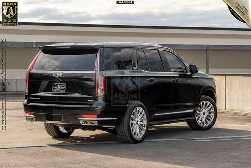 A black Cadillac Escalade Premium Luxury SUV is parked on a rooftop with a cloudy sky in the background. This vehicle appears to be modified by Alpine Armoring.