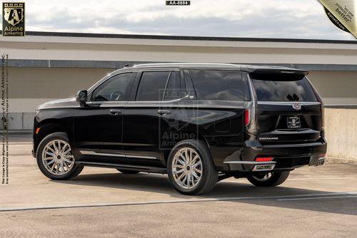 A black, armored Cadillac Escalade Premium Luxury SUV with tinted windows, parked in a rooftop parking lot on an overcast day. The vehicle's brand and model are visible on the rear.