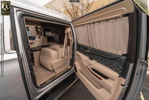 Interior view of a luxury Chevrolet Suburban 3500HD LT VIP Limo's fully open sliding door, showcasing a lavish, beige seating area with curtains and high-end materials.