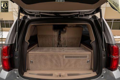 The open trunk of an armored  Chevrolet Suburban 3500HD LT VIP Limo with a large, beige storage compartment inside.