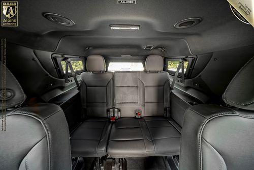 Interior view of an armored Chevrolet Suburban LT SUV showing three rows of black leather seats, seatbelt straps, and side windows.