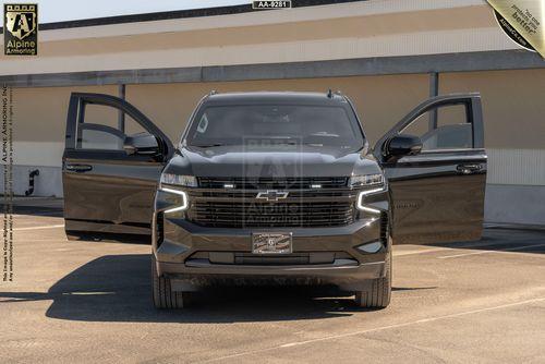 A black Chevrolet Suburban RST SUV with open front and back passenger doors, parked in a sunny outdoor lot near a building.