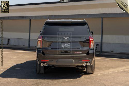 A rear view of a black armored Chevrolet Suburban RST SUV parked in an outdoor parking lot. The vehicle displays a bowtie emblem and "RST" badge on the back.