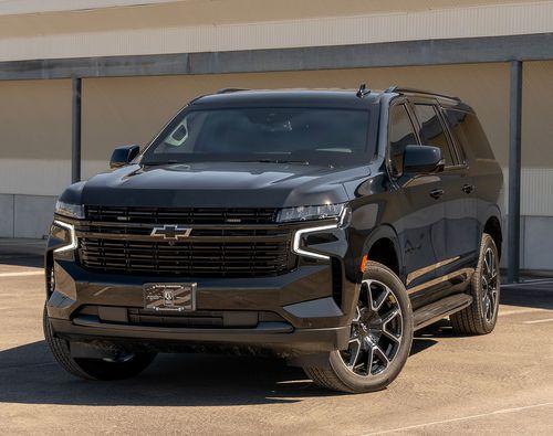 A black armored Chevrolet Suburban RST SUV is parked in an outdoor lot, facing forward.