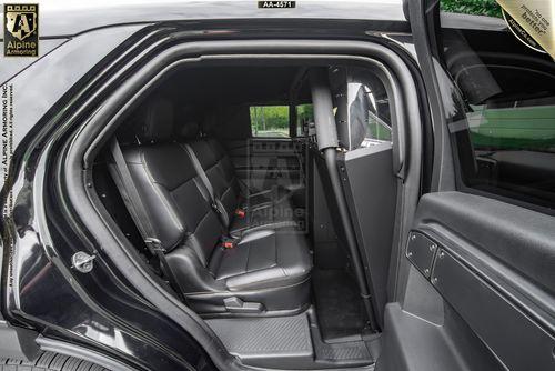 Back seat interior of a black Ford Explorer PPV SUV with leather seats, security partition installed, and partially open door showing the exterior surroundings blurred in the background.