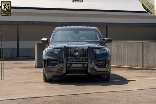 Front view of a black Ford Explorer police SUV with grille guard, parked in an open area with a building and concrete barriers in the background.