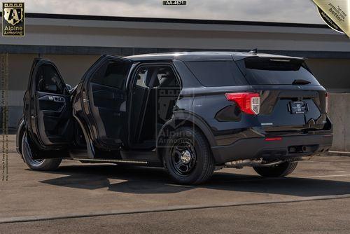 A black armored Ford Explorer PPV SUV SUV with open rear and passenger-side doors is parked on a concrete surface under a cloudy sky. Alpine Armoring branding is visible on and around the vehicle.