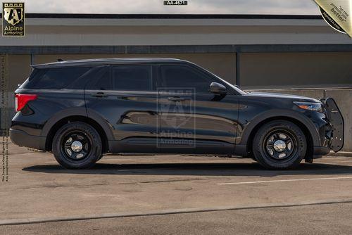 A black bulletproof Ford Explorer SUV with law enforcement markings is parked outside a building. The vehicle has tinted windows, black rims, and a push bumper at the front.