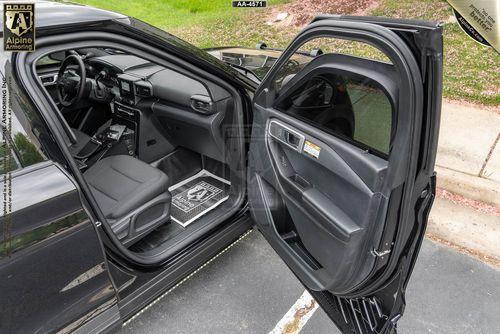 The interior of an open passenger-side door of a black PPV in a parking lot, showcasing the dashboard, steering wheel, and seat, along with visible floor mats and the outer part of the car door.