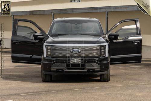 Front view of a black armored Ford Lightning truck with both front doors open. 