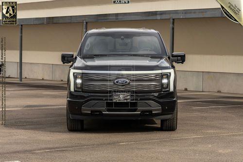 Front view of a black armored Ford Lightning truck. Setting is a parking lot.