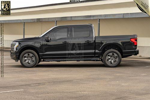 Black armored Ford Lightning truck parked in an empty parking lot in front of a beige building.