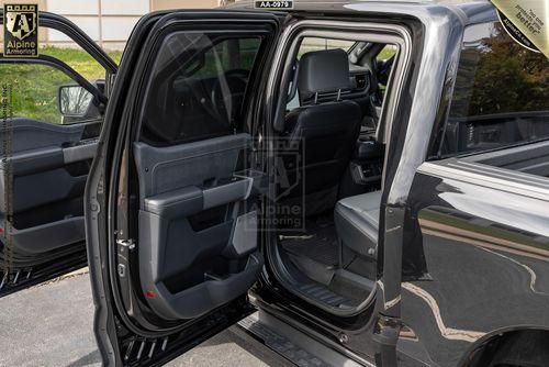 Interior view of the open rear door of a black armored Ford Lightning vehicle, showing two rows of gray seats and various security features visible inside.