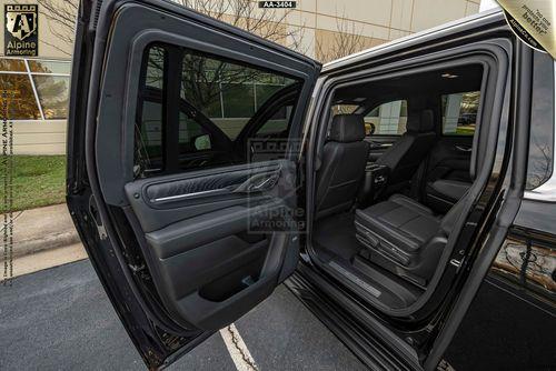 The open rear passenger door of a black armored GMC Yukon Denali XL SUV, displaying the spacious black interior seats and upholstery. The vehicle is parked outside, with a building visible in the background.