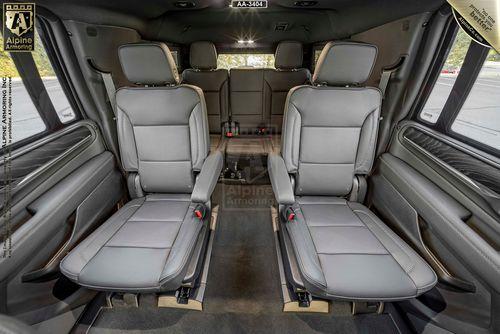 Interior of a GMC armored GMC Yukon Denali XL showing four leather seats, two in the middle row facing forward, and two in the rear. The seats feature armrests, and the car has large windows on the sides.