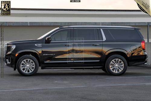 Driver side view of a black armored GMC Yukon Denali SUV parked in front of a building with beige and gray tones. The vehicle has chrome accents and polished wheels.