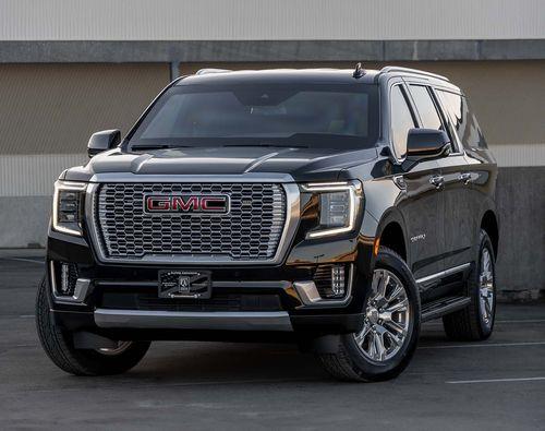 A black GMC Yukon XL from Alpine Armoring parked in a lot. The SUV features a large front grille with the GMC logo, chrome detailing, and sleek headlights.