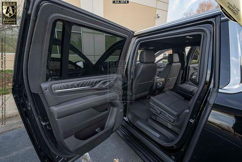 Interior view of a black armored GMC Yukon Denali XL with both rear side doors open, showcasing the seats and interior features.