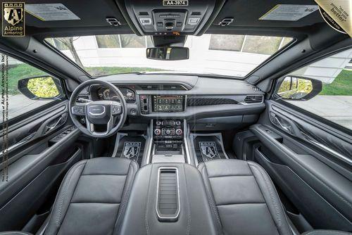 Interior view of a armored GMC Yukon Denali XL SUV featuring a sleek dashboard, a large touchscreen display, leather seats, and various control buttons. "Alpine Amazing" branding is visible.